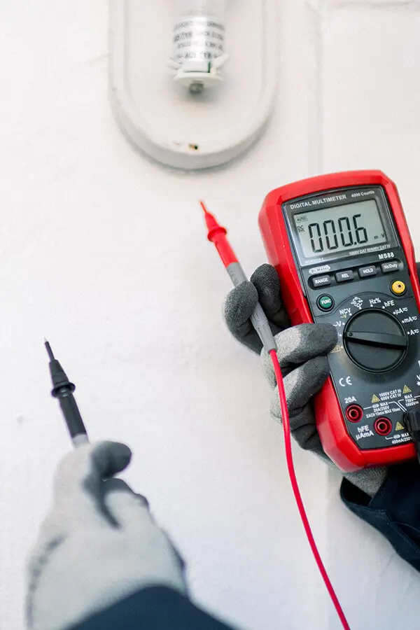 electrician with gloved hands using a multimeter